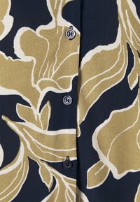 Cárdigan floral en azul marino con grandes patrones florales en beige y verde oliva. Presenta cinco botones redondos negros y una tela suave texturizada.