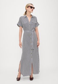 Vestido maxi às riscas, com botões, em preto e branco, mangas curtas dobradas, fendas laterais e um laço na cintura, feito de tecido leve.