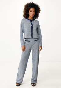 Twee-delige outfit met een geblokte blauw-witte top met knopen en bijpassende broek met zakken en marineblauwe accenten.