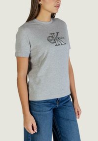 Szary bawełniany t-shirt z czarnym logo "Calvin Klein", o zaokrąglonym dekolcie i krótkich rękawach, w połączeniu z niebieskimi dżinsami.