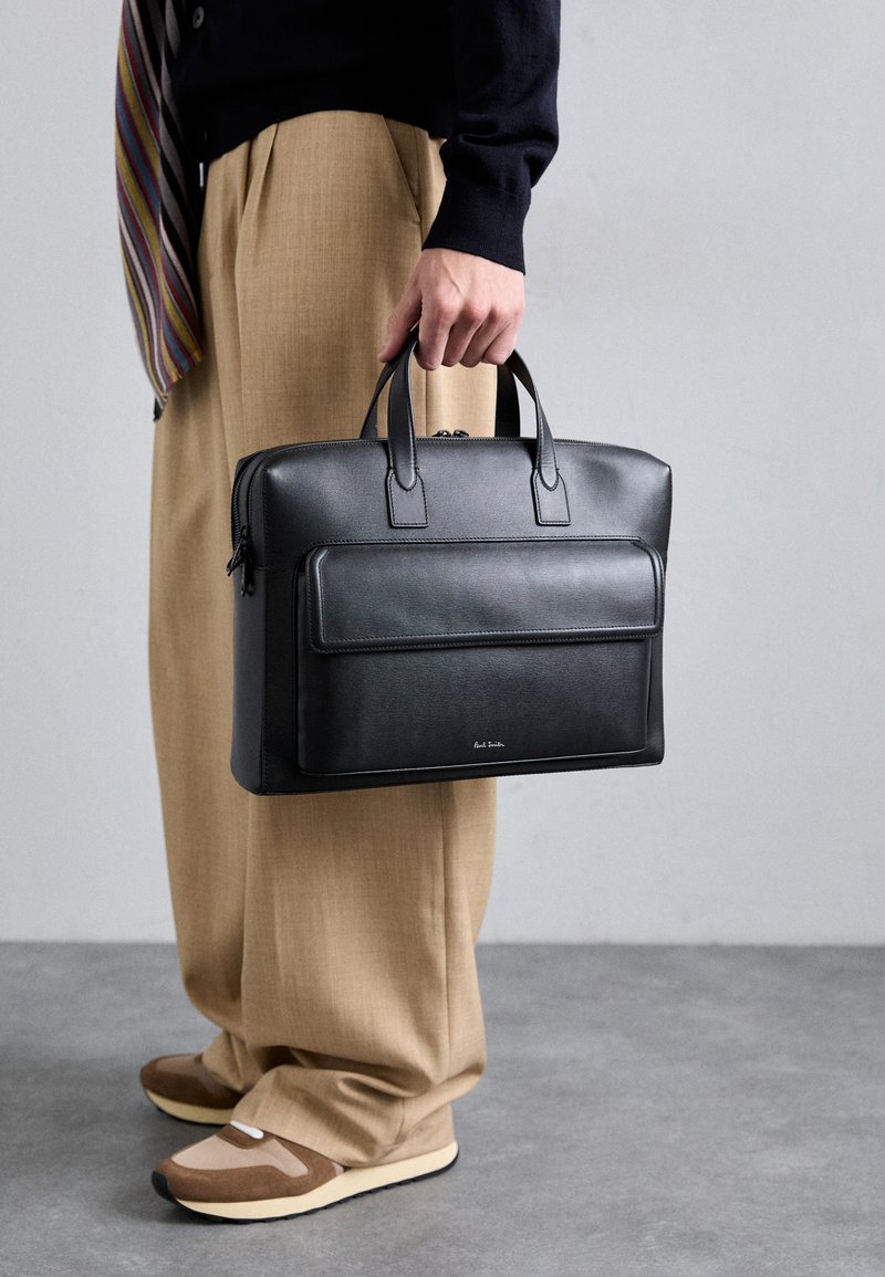 Melnas ādas portfelis ar divām augšējām rokturiem, priekšējo rāvējslēdzēja kabatu un gludu tekstūru. Vienkāršs dizains ar smalku zīmola detaļu.