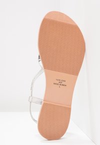 Hopea metallinen, hihnallinen sandaali, jossa on teksturoitu, kuminen pohja. Ominaisuuksiin kuuluu sileä pinta ja uurrettu kuvio jalkapohjassa.