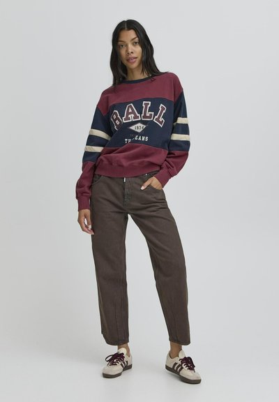 Burgundia ja tumesinine ümmarguse kaelusega dressipluus valgete triipudega. "BALL" graafika ja kuupäeva trükk. Koos pruuni kitsaste pükste ja beežide tossudega.