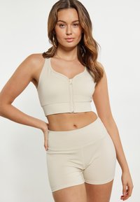 Beige sportovní set obsahující cropped top se zipem vpředu a širokými ramínky, doplněný o odpovídající vysoké šortky, oboje vyrobené z hladkého, elastického materiálu.