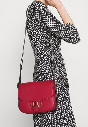 Kvinde iført en sort og hvid kjole med geometrisk mønster og en rød læder crossbody-taske med en gylden RL-logo-lås.