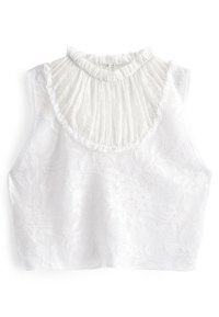 Hvid cropped top lavet af blonderstof, der har en høj, plisseret krave med bølgede kanter. Blomster mønstre pryder den strukturerede overflade.