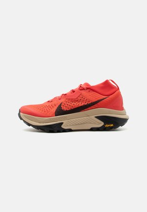 Svetločervená športová obuv s čiernym logom Nike swoosh, béžovou medzipodrážkou, čiernou podrážkou a značkou Vibram na päte.