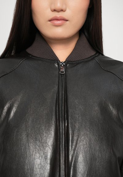 Čierna kožená bomber bunda so zipsom vpredu a ribovaným hnedým golierom. Hladká textúra, zaoblené ramená a neviditeľné bočné vrecká.