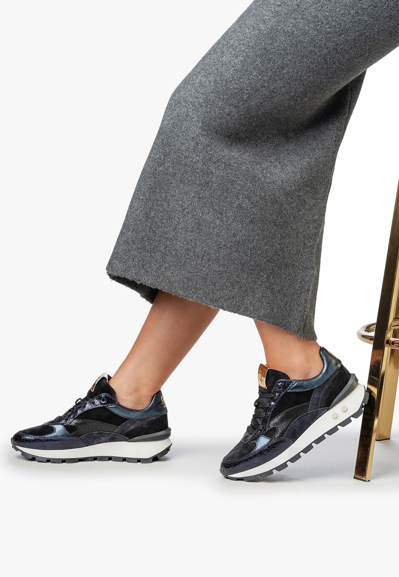 Zapatilla negra y azul marino con un diseño de materiales mixtos, que presenta ante, acentos de cuero y una suela intermedia blanca con un patrón de textura.