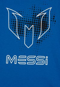 Plava pamučna majica s grafičkim dizajnom koji prikazuje uzorak crnih točaka i bijele stilizirane natpise "MESSi" ispod logoa.
