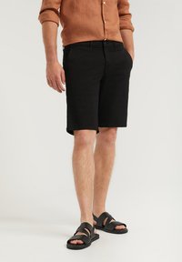 Svarta shorts med rak skärning, tillverkade av lättviktig tyg, tillsammans med svarta sandaler med remmar. Förbättrad med en beige linneskjorta.