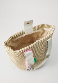 Sac fourre-tout en paille tissée avec des poignées en cuir crème, poche zippée intérieure et étiquettes colorées avec des accents roses et verts.