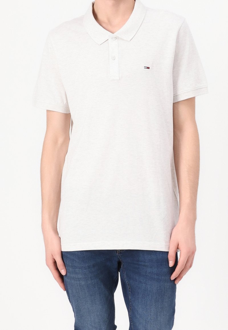 Polo gris clair en tissu doux, avec une patte de boutonnage à trois boutons, des manches courtes et un petit logo brodé sur la poitrine.