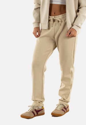Joggers beige con cinturilla elástica y detalle de cordón, combinados con zapatillas beige y maroón que presentan una superficie texturizada y suelas de goma.