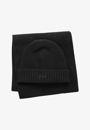 Beanie nera a costine con risvolto e branding discreto. Abbinate a una sciarpa nera a costine coordinata. Entrambi gli articoli presentano una texture.
