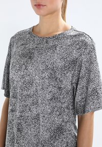 Szara koszulka z melanżowym wzorem w czarno-białe plamki, z okrągłym dekoltem, krótkimi rękawami i luźnym krojem. Wykonana z miękkiego, lekkiego materiału.