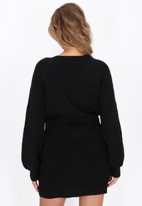 Schwarzes Strickoberteil und Rock-Set mit strukturierten Rautenmuster, gerippten Bündchen und Taillenbund, das ein figurbetontes Design und weiches Material zeigt.