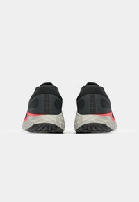 Schwarze Sportschuhe mit einem Obermaterial aus Mesh, die an den Seiten einen roten Akzent und eine strukturierte graue Außensohle für besseren Halt aufweisen.