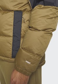 Puffige braune und marineblaue Jacke mit gesteppter Textur, die eine mit Reißverschluss versehenen Tasche und das "700"-Logo am Ärmel aufweist.