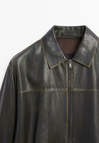 Dark green leather jacket with a structured collar, zip closure, and contrasting stitching, featuring a smooth texture and minimal design.