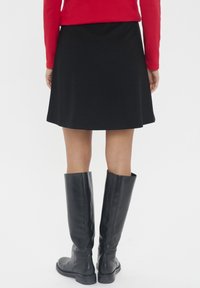 Črn širši krilo z gladko teksturo, kombinirano z črnimi usnjenimi škornji do kolen. Obleka vključuje rdečo dolgosleeve majico.