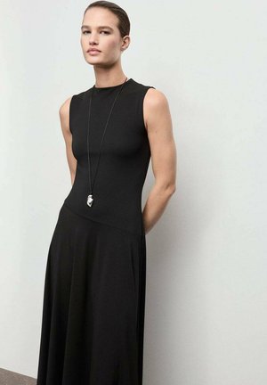 Vestido negro sin mangas, con un cuerpo ajustado que fluye hacia una falda suelta. Tela suave con una textura delicada y un collar con un pendant minimalista largo.