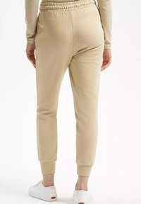 Beżowe dresy o luźnym kroju, z elastycznym pasem i zwężającymi się mankietami. Noszone z białymi trampkami, charakteryzującymi się gładką fakturą.