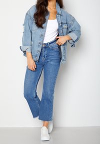 Vaaleansininen farkkutakki kulutuksilla, valkoinen t-paita, korkeavyötäröiset siniset farkut ja valkoiset tennarit, jotka esittävät rentoa tyyliä.