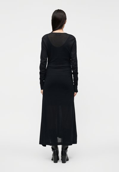 Μαύρο φόρεμα με μακριά μανίκια από απαλό, ελαφρύ υλικό. Διαθέτει ελαφρώς διάφανο πίσω μέρος και εφαρμοστή μέση, συνδυασμένο με μπότες μέχρι το γόνατο.