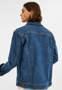 Tummansininen farkkutakki klassisella kauluksella, näkyvillä saumoilla sekä napitakkiratkaisuilla hihansuissa ja helmassa. Mukautuu rentoon istuvuuteen.