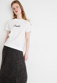Weißes Baumwoll-T-Shirt mit dem Text "Dream" in Schwarz, kombiniert mit einem langen, strukturierten grauen Rock mit einem schwarzen Leopardenmuster.