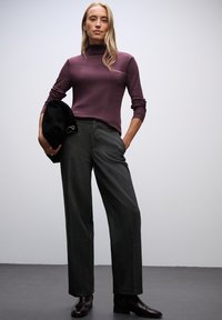 Maglione a maniche lunghe, aderente, color viola scuro abbinato a pantaloni a gamba larga grigio scuro a vita alta e stivaletti neri. Tiene un berretto nero.