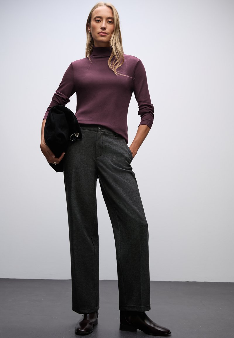 Maglione a maniche lunghe, aderente, color viola scuro abbinato a pantaloni a gamba larga grigio scuro a vita alta e stivaletti neri. Tiene un berretto nero.