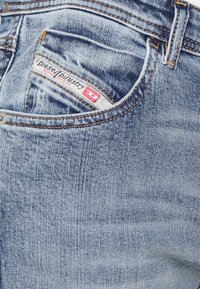 Jeans de mezclilla azul claro con una textura desgastada, con costuras naranjas y una etiqueta de marca roja y blanca en el bolsillo trasero.