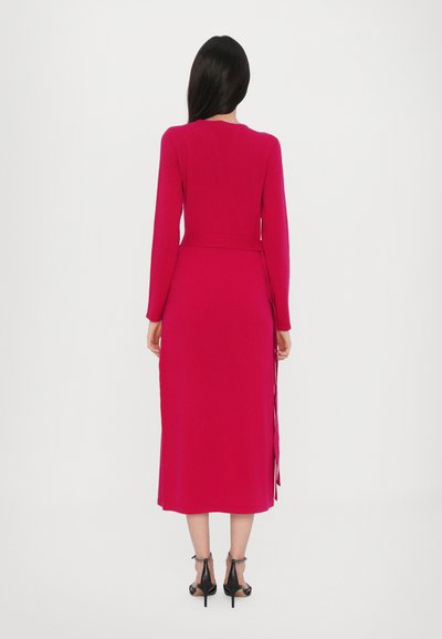 Rochie mulată cu mâneci lungi dintr-un material roz aprins, cu lungime până la jumătatea gambei, detaliu cu panglică laterală și textură netedă. Tocuri negre vizibile.