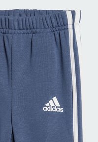 Pantalones deportivos azul marino con rayas blancas a los lados y una cinturilla elástica. Presenta un pequeño logotipo blanco de Adidas en la pierna izquierda.