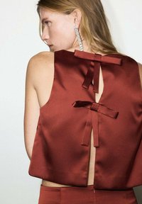 Top en satin de couleur rouille avec un col montant et un dos découpé, présentant deux petits nœuds en bas de la découpe pour le détail.