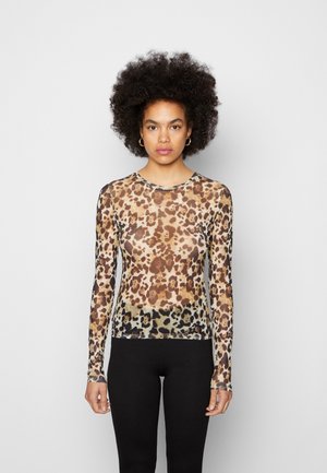Haut à manches longues en tissu transparent à imprimé léopard, avec un col rond. Il arbore un mélange de taches marron, beige et noires. Accompagné de leggings noirs.
