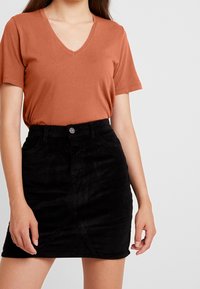 En rostfärgad V-ringad t-shirt i kombination med en svart kordflöjlskjol med framknappsstängning och diagonala sömdetaljer.