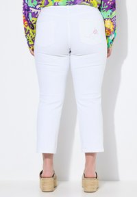 Valkoiset lyhyet farkut, joissa on tiukka muotoilu, sisältäen kaksi takataskua, joista toisessa on vaaleanpunaista brodointia. Kangas näyttää sileältä ja farkkumaiselta.