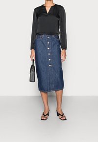 Svart satinblus med lång ärm och V-ringning, kombinerad med en midikjol i denim med knappfront som har fem knappar och framfickor. Svarta klacksandaler.