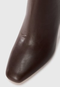 Brown leather ankle boot with a square toe, smooth texture, and minimal detailing. The surface shows slight creases for added character.