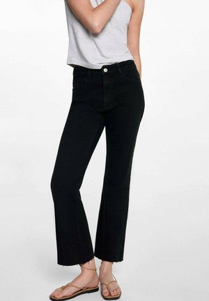 Svarta hög midja jeans med rak ben, fransad fåll, gjorda av denimtyg, tillsammans med en grå ärmlös topp och bruna sandaler.