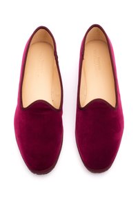 Scarpe slip-on in velluto bordeaux con una texture liscia, punta arrotondata e bordo scuro a contrasto lungo i bordi. Interno con fodera di colore chiaro.
