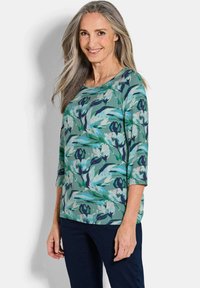 Bluse mit floralem Druck in Grün, mit Rundhalsausschnitt, Dreiviertelärmeln und legerem Schnitt. Das Design beinhaltet blaue und marineblaue Akzente.