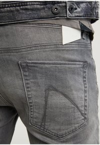 Jeans de mezclilla gris con cierre de botón, diseño distintivo de los bolsillos traseros y etiqueta de marca de cuero blanco en la cintura.
