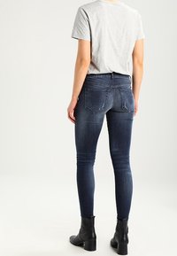 Tummansiniset skinny-farkut, joissa on sileä pinta, varustettuna takataskuilla ja tiukalla muotoilulla, yhdistettynä vaaleanharmaaseen t-paitaan ja mustiin nilkkabootseihin.