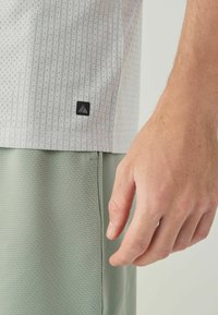 Short-sleeved, light gray shirt with a textured pattern and a black logo tag; paired with mint green textured shorts. Hand shown on side.