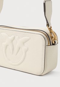 Bolsa de couro crème com design em relevo, fecho dourado e alça de ombro. Forma retangular com bordas arredondadas, apresentando detalhes de costura.