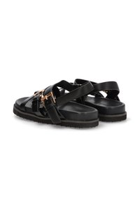 Sandalias negras con múltiples tiras cruzadas, que presentan detalles metálicos y una suela texturizada. Están hechas de material sintético, diseñadas para ser fáciles de poner y quitar.